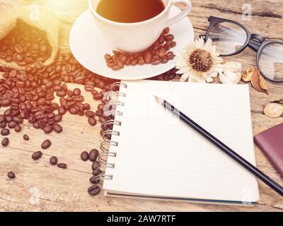 Tazza di caffè con chicco di caffè e notebook con una matita su un tavolo di legno. caffè menu sfondo per bar o caffetteria Foto Stock