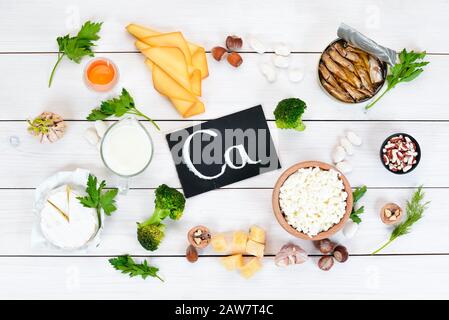 Cibo con calcio. Una varietà di alimenti ricchi di calcio: Formaggio, latte, parmigiano, panna acida, pesce, mandorle, prezzemolo, aglio, broccoli. Su un legno bianco Foto Stock