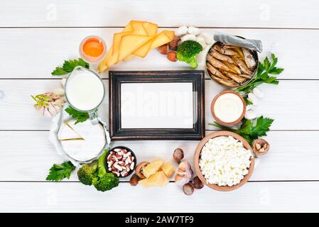 Cibo con calcio. Una varietà di alimenti ricchi di calcio: Formaggio, latte, parmigiano, panna acida, pesce, mandorle, prezzemolo, aglio, broccoli. Su un legno bianco Foto Stock