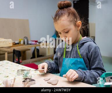 Una ragazza di 6 anni fa il suo mestiere di argilla - un cuore come un dono per la mamma, master class in un laboratorio di ceramica Foto Stock