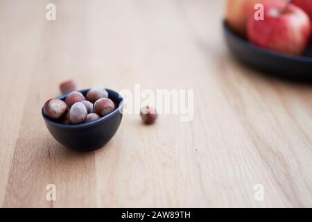 Nocciole in una ciotola di colore scuro su legno di quercia con mele rosse sullo sfondo Foto Stock