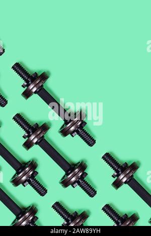 Immagine verticale sportiva. Dumbbells su sfondo verde menta. Disposizione piatta, vista dall'alto, spazio di copia. Foto Stock