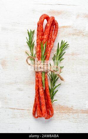 Salsiccia secca con rosmarino su fondo bianco legno. Kabanosy. Vista dall'alto. Spazio libero per il testo. Foto Stock