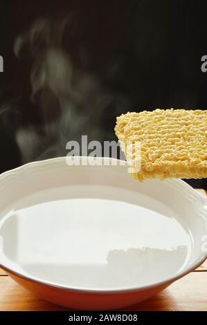 spaghetti istantanei che galleggiano sull'acqua calda nel recipiente e condendo la polvere di condimento Foto Stock