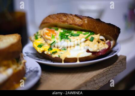 panino arrosto con salsiccia, uova, formaggio e cipolle verdi. panino con doppio pane tostato succoso. Foto Stock