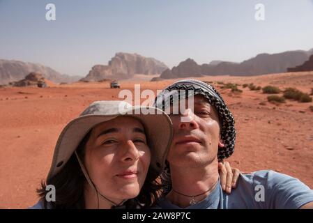 Coppia fare una foto selfie nel deserto di Wadi Rum, Giordania. Donna che indossa cappello e l'uomo una sciarpa keffiyeh Palestinain Foto Stock