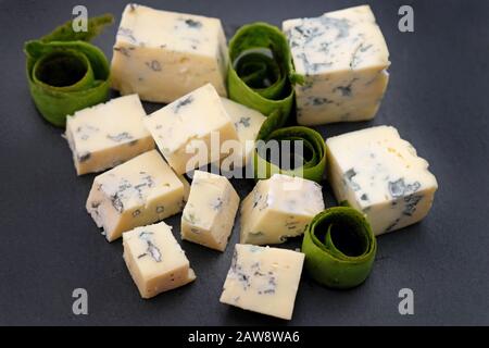 Cubetti di formaggio blu su sfondo nero. Formaggio blu su una tavola di ardesia. Formaggio Roquefort su un piatto. Foto Stock