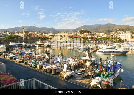 Vista panoramica sul porto con una fila di barche da pesca ormeggiate al molo, yacht di lusso e la città costiera sullo sfondo, Sanremo, Liguria, Italia Foto Stock