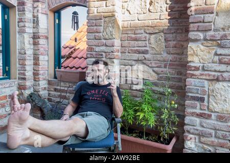 uomo seduto a casa all'aperto e fumare erbacce Foto Stock