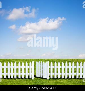 Una recinzione bianca in picchetto e porta aperta che conduce ad un bel campo verde e cielo blu in estate Foto Stock