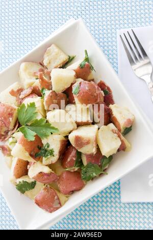 Insalata di patate sana fatta con patate nuove, pancetta di tacchino, oli, erbe e spezie varie. E' servito su un piatto quadrato bianco. Foto Stock