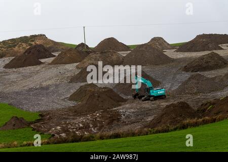 Scavatore meccanico che schiarimento rocce da un campo in Irlanda. Foto Stock