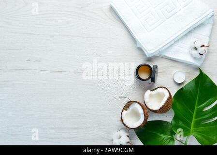 Cosmetici a base di cocco e foglie tropicali. Su uno sfondo di legno bianco. Disposizione piatta. Foto Stock
