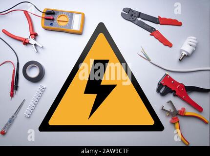 Vari Strumenti Per Elettricisti Intorno Al Segnale Ad Alta Tensione Su Sfondo Grigio Foto Stock