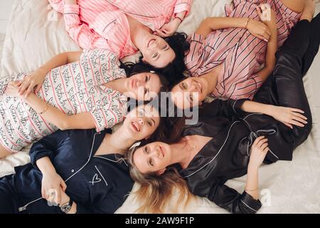 Vista dall'alto del gruppo di donne piuttosto giovani in pigiami sdraiati a letto e divertirsi. Concetto di festa di compleanno Foto Stock