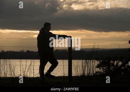 Lochwinnoch, Renfrewshire, Scozia, Regno Unito. 7th Febbraio 2020 UN pendolari guarda a sud verso il tramonto sul lago Barr a Lochwinnoch. Un avvertimento meteo giallo è stato emesso con forti venti previsti il Sabato pomeriggio e la sera può portare ad un certo disturbo. Ci si aspetta qualche ritardo per viaggiare su strada, in treno e in traghetto, con condizioni peggiorate dalla pioggia battente, dall'acqua di superficie e dal credito spray: Chris McNulty/Alamy Live News Foto Stock