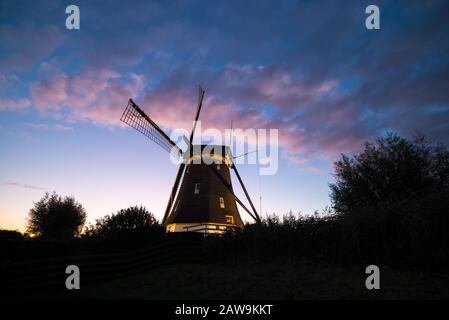 Bella immagine di un mulino a vento illuminato olandese e nuvole colorate al tramonto Foto Stock