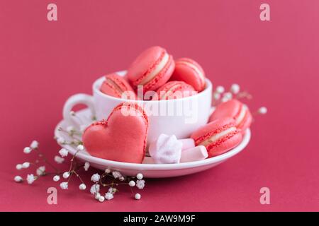 Sfondo di San Valentino con macaroni rosa a forma di cuore e marshmallows. Tazza con macaroni e marshmallows. Foto Stock