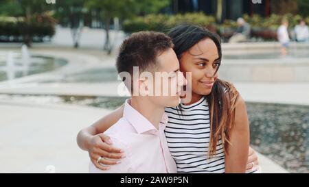 Bell'uomo e bella donna nera che hanno data in un moderno parco cittadino. Parlano e l'uomo la mostra qualcosa intorno. Foto Stock