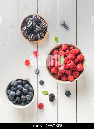 tre ciotole con frutti di bosco, lampone, mirtilli, more, su sfondo di legno bianco Foto Stock