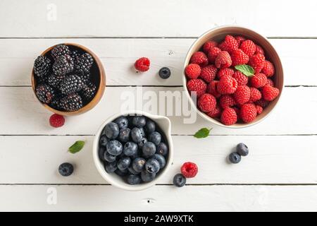 tre ciotole con frutti di bosco, lampone, mirtilli, more, su sfondo rustico di legno Foto Stock