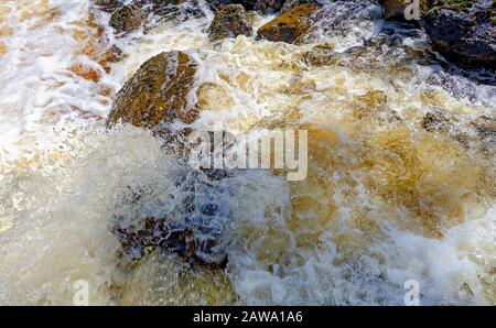 Schiuma e spruzzi d'acqua bianca color oro che traboccano di rocce in Svezia Foto Stock