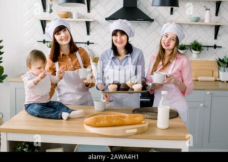 Bambina piccola è seduta sul tavolo in cucina e divertirsi. Nonna e le sue figlie stanno bevendo caffè e mangiando muffin. Donne felici Foto Stock