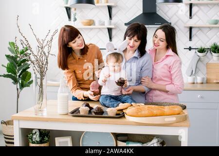 Soddisfatto Famiglia con nonna, due figlie e bambina che si gode passatempo di pasqua e mangiare cupcakes. Una bambina ha orecchie di coniglio su Foto Stock