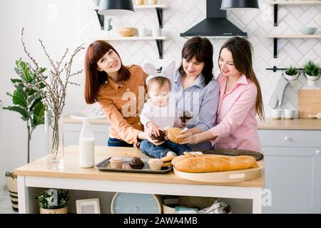 Soddisfatto Famiglia con nonna, due figlie e bambina che si gode passatempo di pasqua e mangiare cupcakes. Una bambina ha orecchie di coniglio su Foto Stock