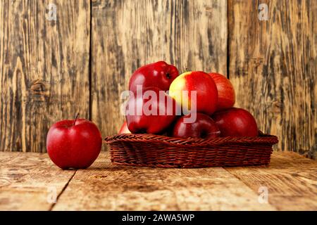 Le mele rosse mature si trovano in un cestino di vimini su un vecchio tavolo di legno su uno sfondo di legno, immagine con spazio di copia. Foto Stock