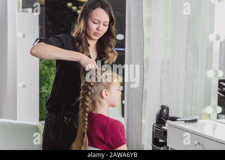 Il parrucchiere tessera una treccia ad una ragazza bionda pre-teen Foto Stock