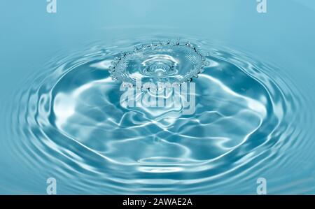 Gocce di acqua pulita e fresca cadono da un'altezza di acqua blu trasparente che forma schizzi sotto forma di figure originali. Foto Stock