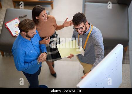 responsabile delle vendite che mostra a una giovane coppia le opzioni per il loro disegno interno domestico su un pannello. mostrando, spiegando, il concetto di persuasione Foto Stock