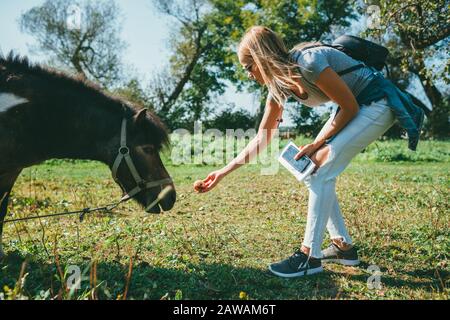 Bella giovane bionda dai capelli lunghi in una T-shirt rosa, jeans blu chiaro e legato alla giacca in denim hips, piegato e alimentare una mela a a. Foto Stock