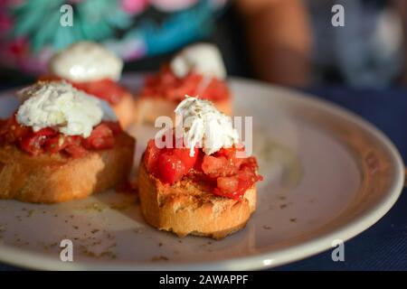 Un piatto di bruschetta con pomodori sul pane cotto e un cucchiaio di ricotta montata sulla parte superiore da un caffè sul marciapiede a Vernazza Italia Foto Stock