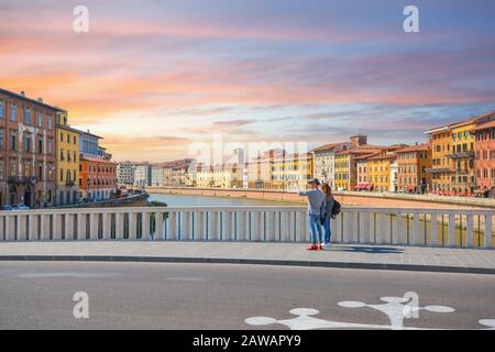 Una giovane coppia si ferma su un ponte sul fiume Arno per scattare foto selfie nella città toscana di Pisa in una calda giornata estiva. Foto Stock