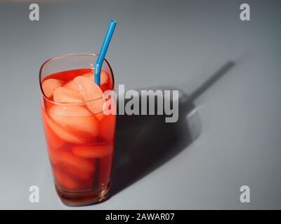 closeup di vetro di punzone di frutta rossa con cubetti di ghiaccio e la paglia blu gettando un'ombra Foto Stock