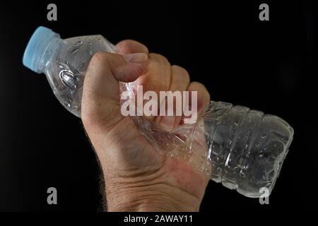 Una bottiglia di plastica vuota schiacciata da una mano mans. Foto Stock