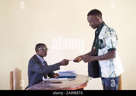 Un uomo d'affari africano di successo e uno studente che consegna la sua carta d'identità per identificare la sua azienda in un ufficio Foto Stock