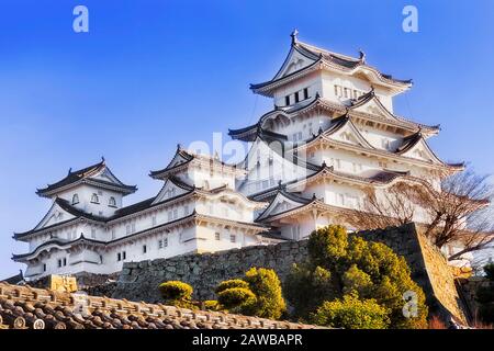 Castello storico dipinto di bianco nella città giapponese Himeji su pareti di pietra sotto il cielo blu. Foto Stock