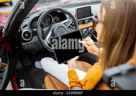 Giovane donna che usa un tablet digitale mentre è seduto in auto, guarda dal retro sul tablet con schermo nero per copiare la pasta Foto Stock