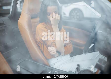 Giovane donna sensazione di stress, avendo un mal di testa mentre seduto sul sedile del conducente della auto convertibile. Vista attraverso il parabrezza Foto Stock
