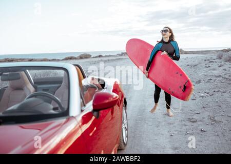 Ritratto di una giovane donna surfista in costume da bagno a piedi con tavola da surf sulla strada sterrata vicino all'oceano. Stile di vita attivo e concetto di surf Foto Stock