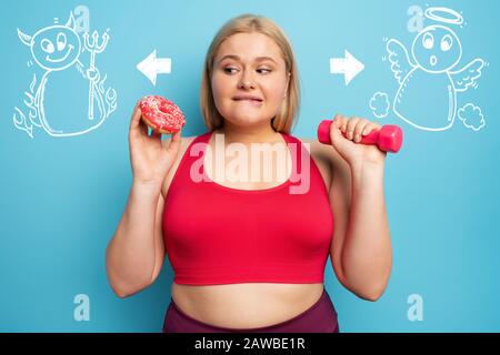 Fat ragazza pensa di mangiare ciambelle invece di fare palestra. Concetto di indecisione e dubbio con angelo e suggerimento del diavolo Foto Stock