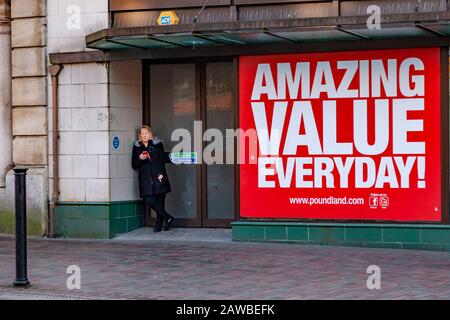 Femmina in piedi nella porta fumatori e sul telefono cellulare fuori Poundland in Abington Street, Northampton, Inghilterra, Regno Unito. Foto Stock