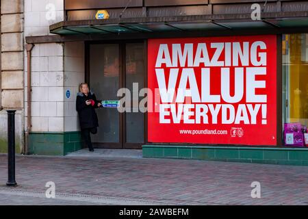 Femmina in piedi nella porta fumatori e sul telefono cellulare fuori Poundland in Abington Street, Northampton, Inghilterra, Regno Unito. Foto Stock