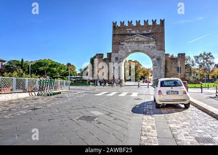 Rimini, Italia - 20 ottobre 2019: Arco di Augusto con auto parcheggiata e noleggio scooter elettrici in primo piano Foto Stock