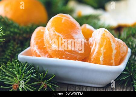 Fette di mandarino giallo maturo si trovano in una ciotola accanto ai rami verdi di un albero di Natale. Agrumi, tangerini o arance. Primo piano. Foto Stock