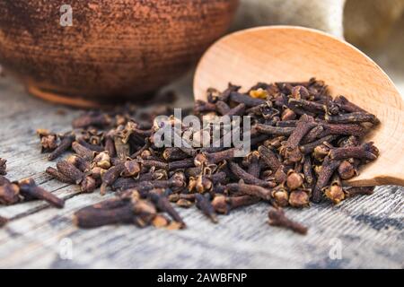 Una spezia di chiodi di garofano secchi si trova su un cucchiaio di legno ed è sparsa su vecchie tavole di legno. Spezie chiodi di garofano per cucinare. Primo piano. Foto Stock