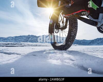 Primo piano di una ruota fatbike, rotolando su un lago di montagna ghiacciato. Viaggiare in inverno. Spedizione estrema. Foto Stock
